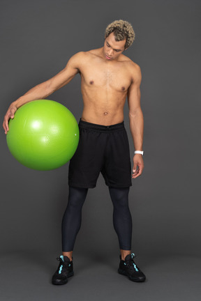 Front view of a shirtless afro man holding a big green gym ball