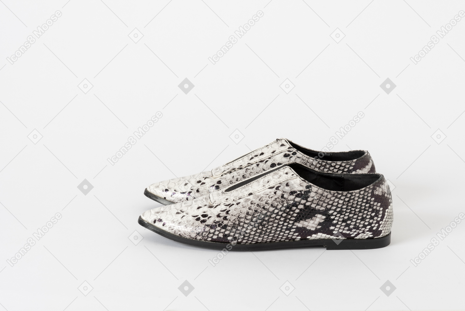 A side shot of a pair of white & black snakeskin flat shoes