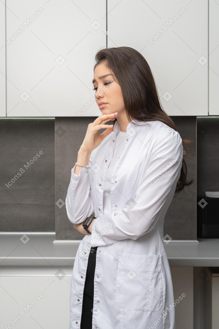 Three-quarter view of a doubting miserable female doctor touching chin