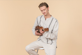 Young caucasian man sitting and playing on guitar