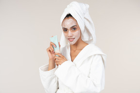 Black woman in white bathrobe and head towel enjoying her skin care routine