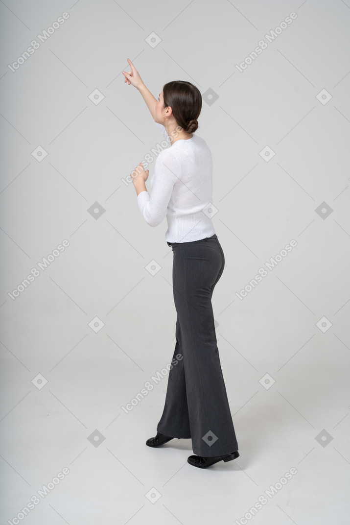 Side view of a woman in black pants and white blouse pointing up with a finger