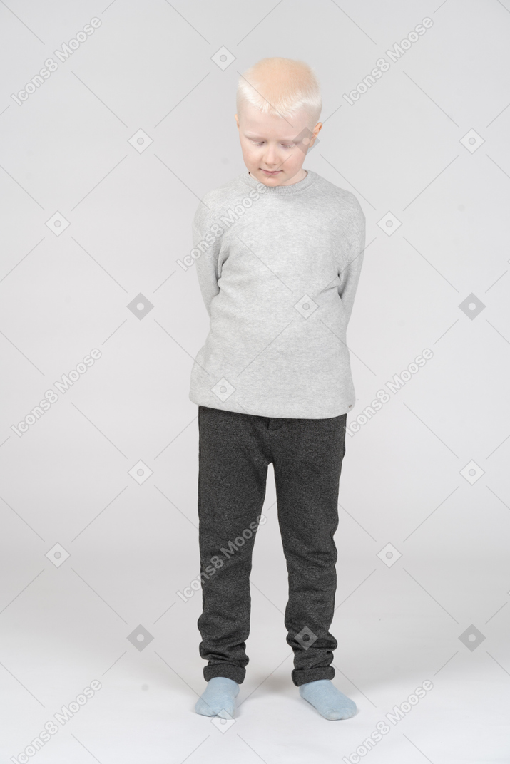 Little boy looking down with his arms behind back