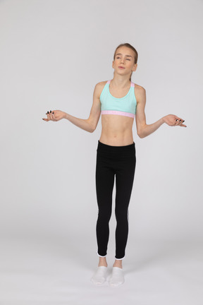 Вид спереди девушки-подростка в спортивной одежде, поднимающей руки и рассуждающей