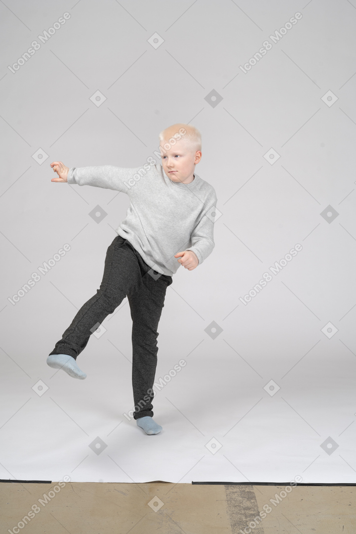 Вид спереди мальчика в повседневной одежде, пинающего ногу