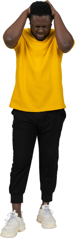 Vista frontal de un joven de piel oscura con camiseta amarilla tocando la cabeza