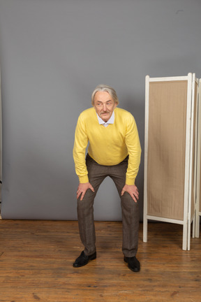 Front view of a curious old man leaning forward while putting hands on legs