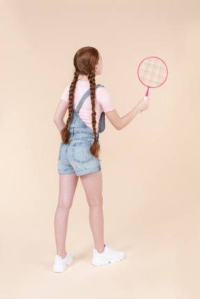 Teenage girl holding tennis racket and standing back to camera