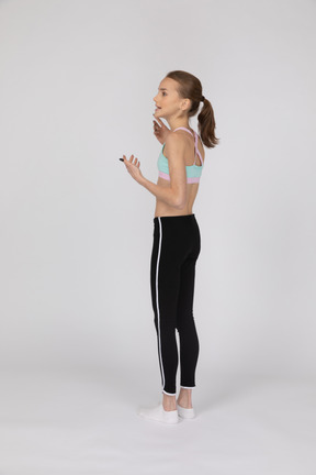 Three-quarter back view of a teen girl in sportswear raising hands and looking aside