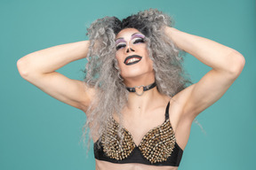 Drag queen en soutien-gorge clouté souriant avec les mains dans les cheveux