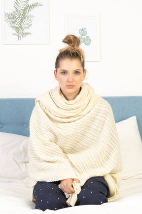 Front view of a young lady wrapped in white blanket sitting in bed