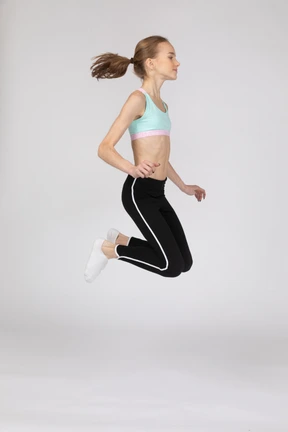 Vista lateral de una jovencita en ropa deportiva en cuclillas y poniendo las manos en las caderas