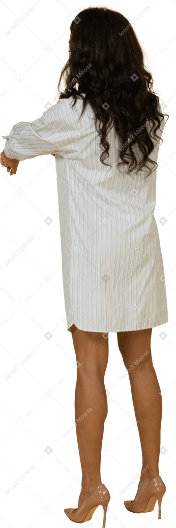 Three-quarter back view of a dark-skinned young female in white dress rolling up her sleeves