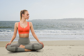 A woman sitting in a yoga position on the beach