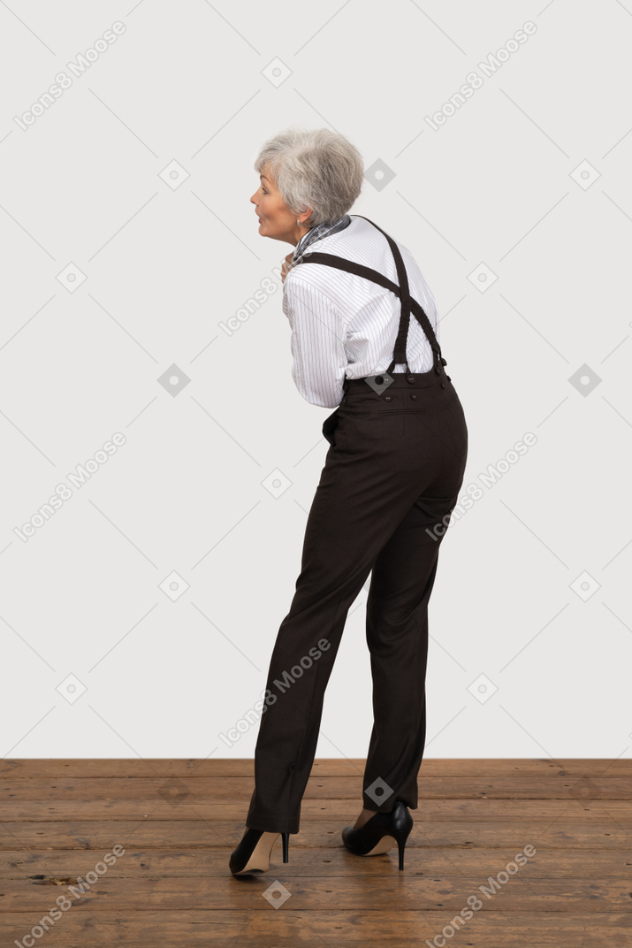 Three-quarter back view of an old lady in office clothing holding hands together while leaning forward