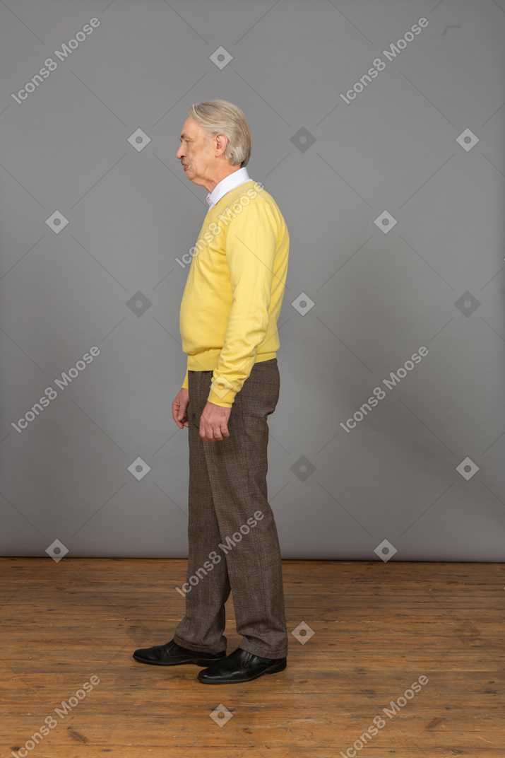 一个不高兴的老人，在一件黄色的套衫，放在一边看的侧视图