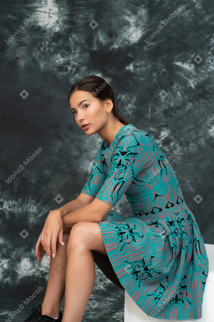 Tired woman in turquoise dress sitting on a cube