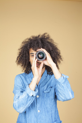 Man in denim suit holding a camera next to his face