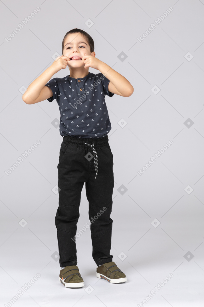Vista frontal de um lindo garoto colocando os dedos na boca e mostrando a língua