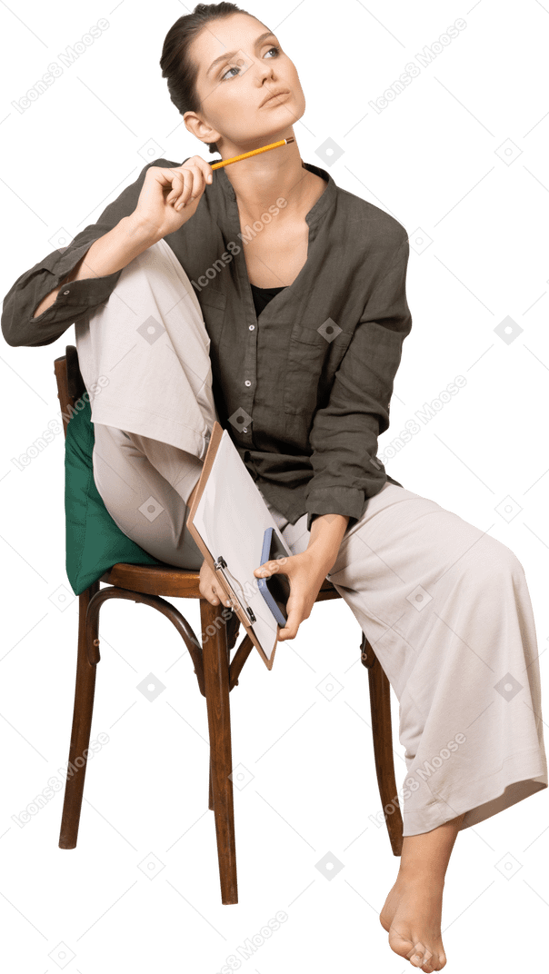 Vista frontale di una giovane donna premurosa che indossa abiti da casa seduta su una sedia e prende appunti