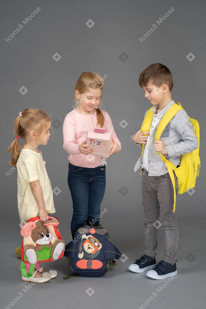 Três crianças com mochilas e brinquedos fofos