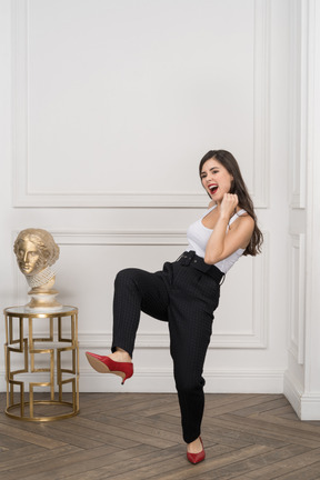 Full-length of an energetic young female kicking while standing near golden greek sculpture