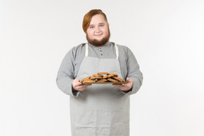 Un gros boulanger souriant tenant une assiette de biscuits