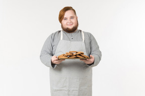 Um padeiro gordo sorridente segurando um prato de biscoitos