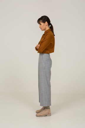 Vista lateral de una mujer asiática joven cansada en calzones y blusa cruzando los brazos