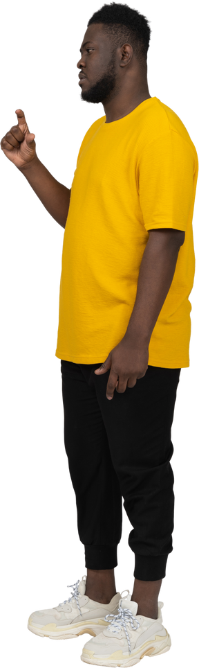 Vista de três quartos de um jovem de pele escura em uma camiseta amarela mostrando o tamanho de alguma coisa