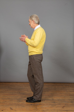 Вид сбоку аплодирующего старика в желтом пуловере, смотрящего в сторону