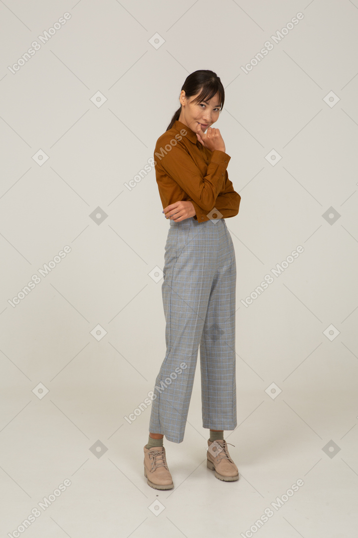 Vista de três quartos de uma jovem mulher asiática adivinhando calções e blusa tocando os lábios