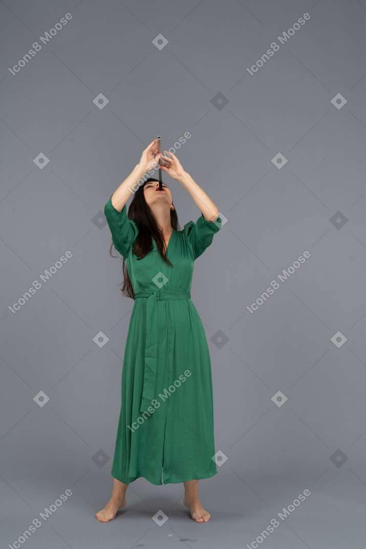 Front view of a young lady in green dress playing flute while leaning back