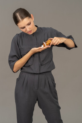 Vista frontale di una giovane donna in tuta che versa le pillole da un barattolo