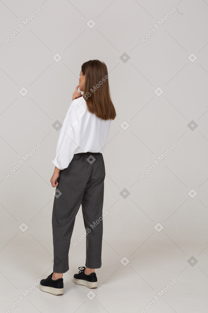 彼女の指を噛んでいるオフィスの服を着た若い女性の4分の3の背面図