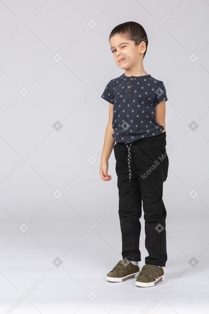 Front view of a cute boy standing with hands behind back and making faces
