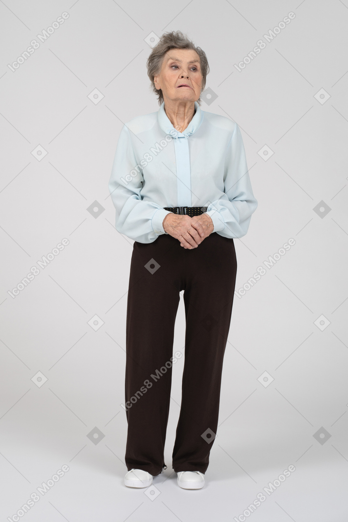 Vue de face d'une vieille femme grimaçant usuellement avec les mains jointes