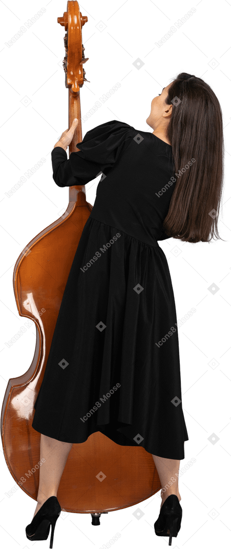 Vista posterior de un joven músico en vestido negro sosteniendo su contrabajo