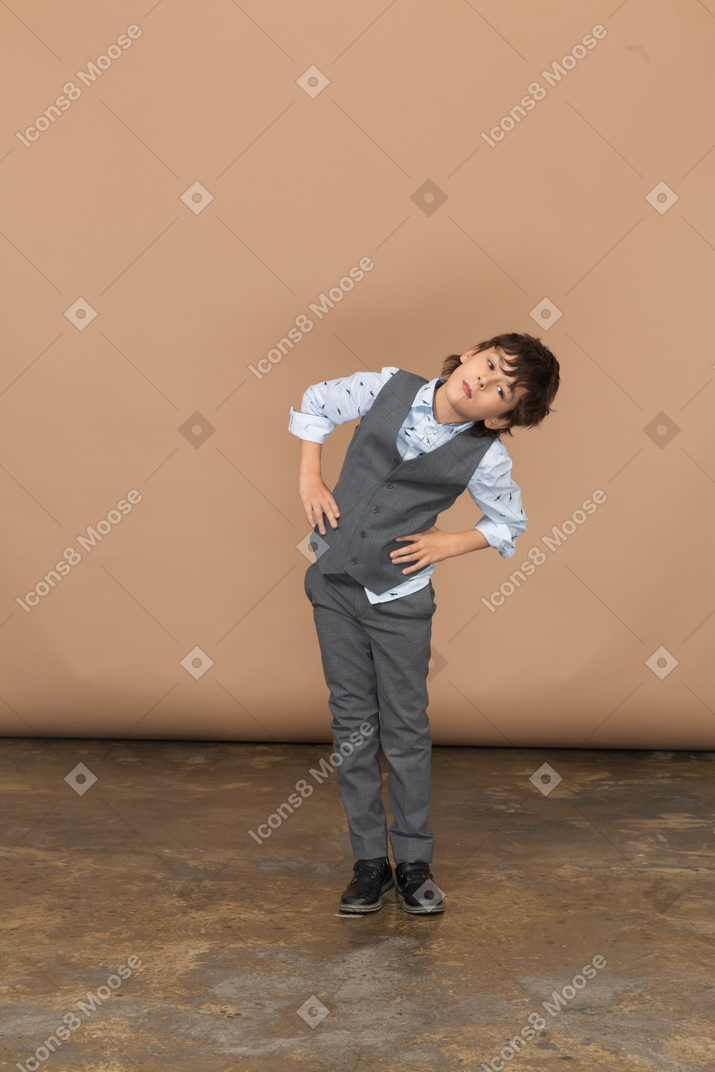Вид спереди мальчика в сером костюме, стоящего с руками на бедрах