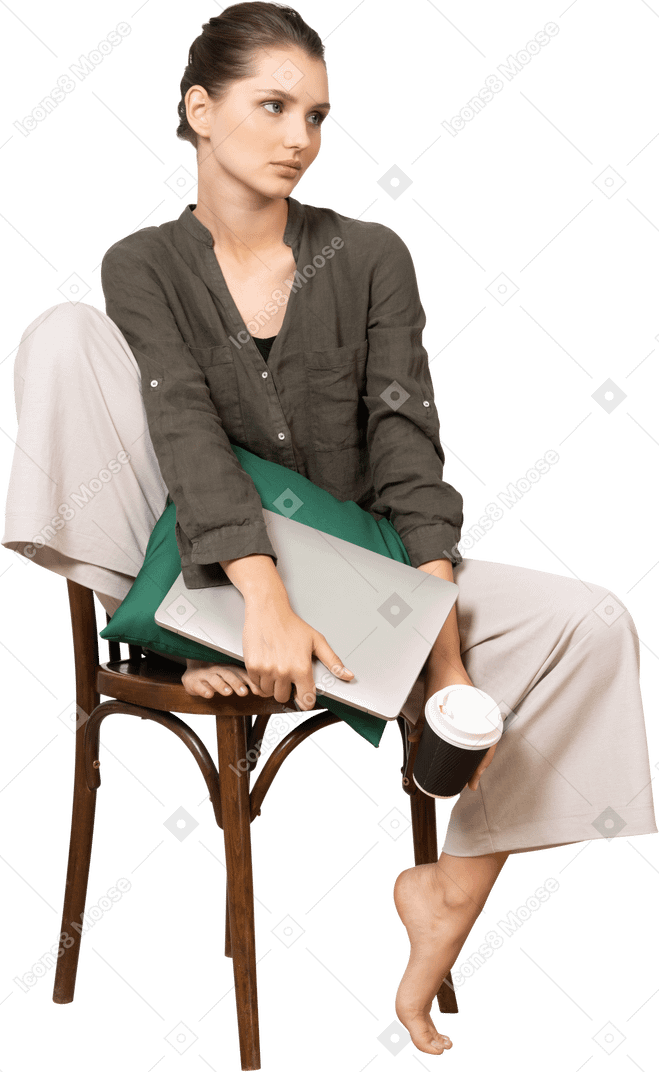 Front view of a young woman sitting on a chair and holding her laptop & touching coffee cup