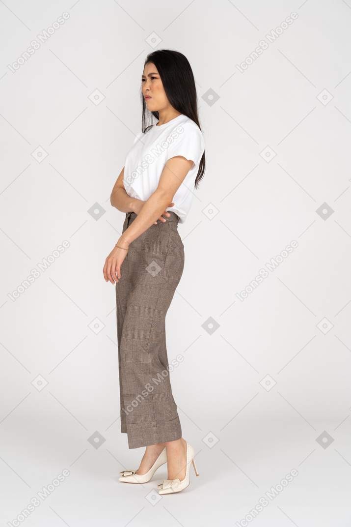 Vista di tre quarti di una giovane donna con una smorfia scontenta in calzoni e maglietta