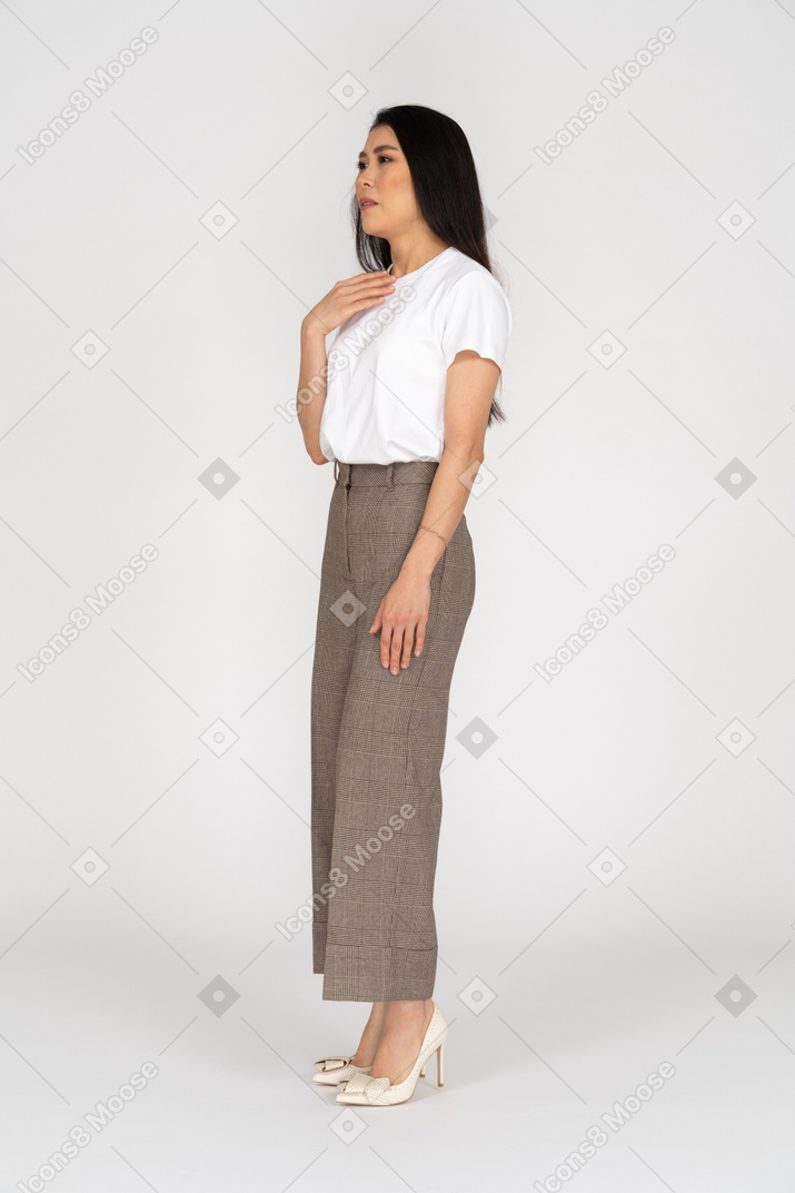 Vista di tre quarti di una giovane donna in calzoni e maglietta che si toccano il petto