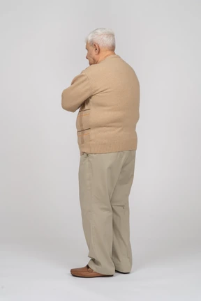 Side view of an old man in casual clothes standing with crossed arms