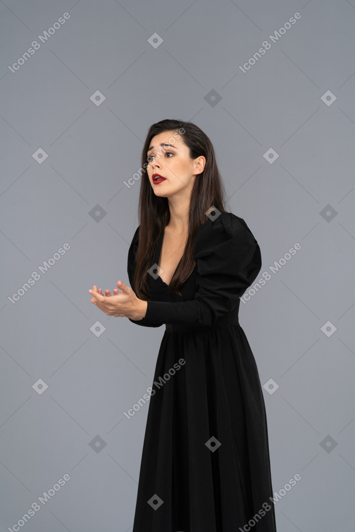 Three-quarter view of a worried gesticulating young woman in black dress