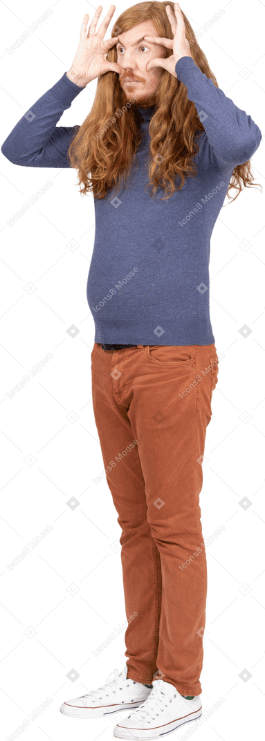 Vista lateral de un joven con ropa informal mirando a través de los dedos