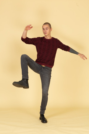 Front view of a balancing young man in red pullover raising hands