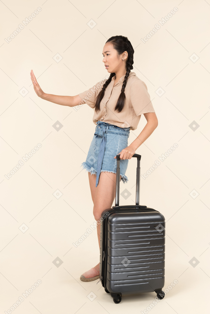 Young asian traveller standing near suitcase and showing stop sign