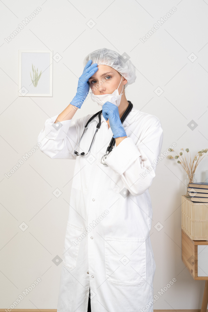Vista de três quartos de uma jovem médica colocando uma máscara e olhando para a câmera