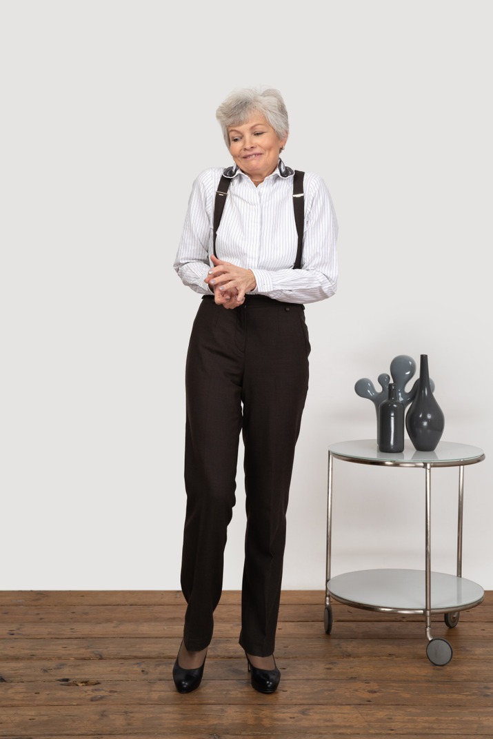 Front view of a perplexed old lady in office clothing holding hands together