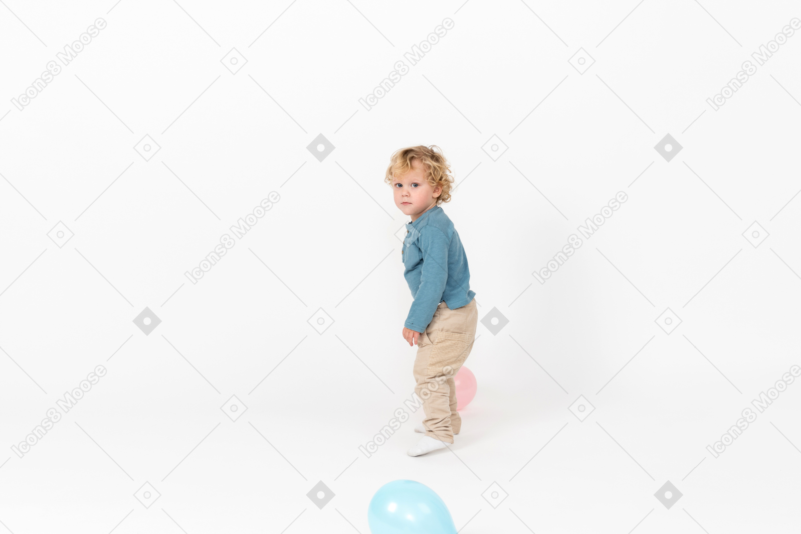 Baby boy standing among balloons and looking into camera